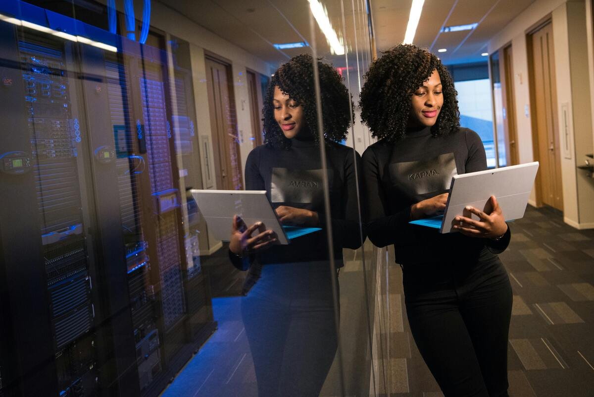 A woman working on a laptop in a server room with data servers in the background.