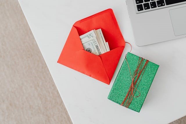 An envelope with cash and a gift box next to a laptop, symbolizing the ease of receiving a Direct Deposit Bonus