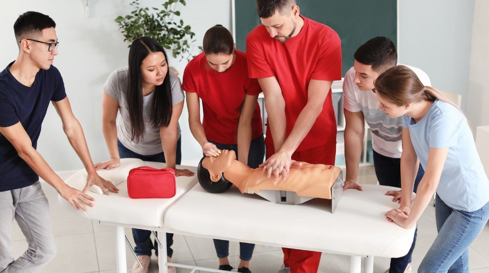 Paramedic education students practicing CPR on a mannequin during a hands-on training session, learning vital life-saving skills in a classroom setting.