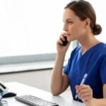 Nurse providing triage services over the phone while using a computer, offering professional after-hours care