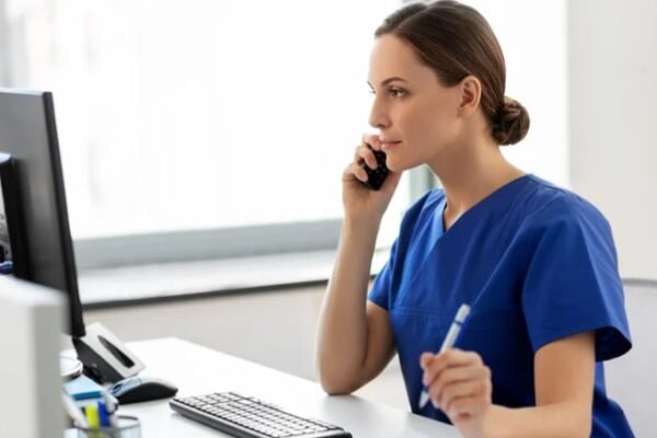 Nurse providing triage services over the phone while using a computer, offering professional after-hours care