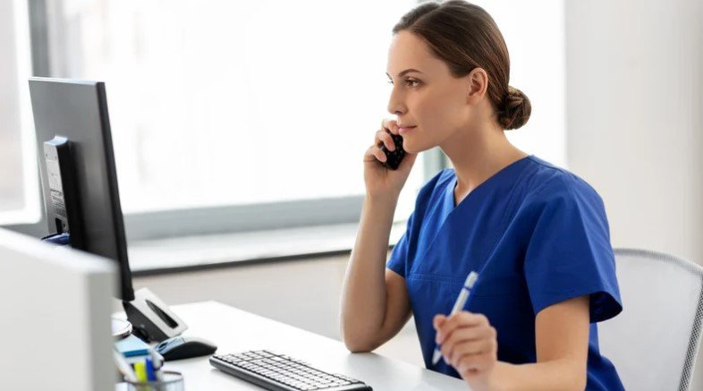 Nurse providing triage services over the phone while using a computer, offering professional after-hours care