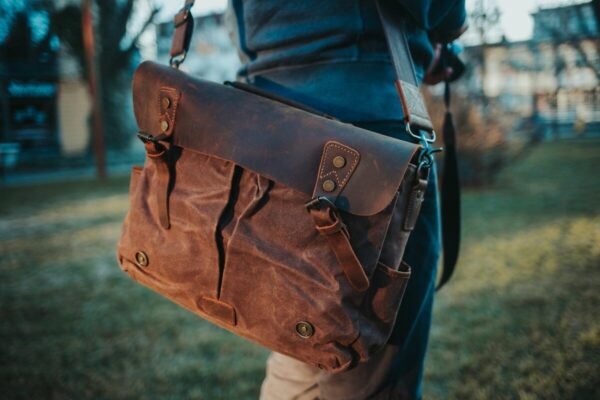 A person carrying the perfect bag, a stylish brown leather satchel with a mix of canvas, in a serene outdoor setting