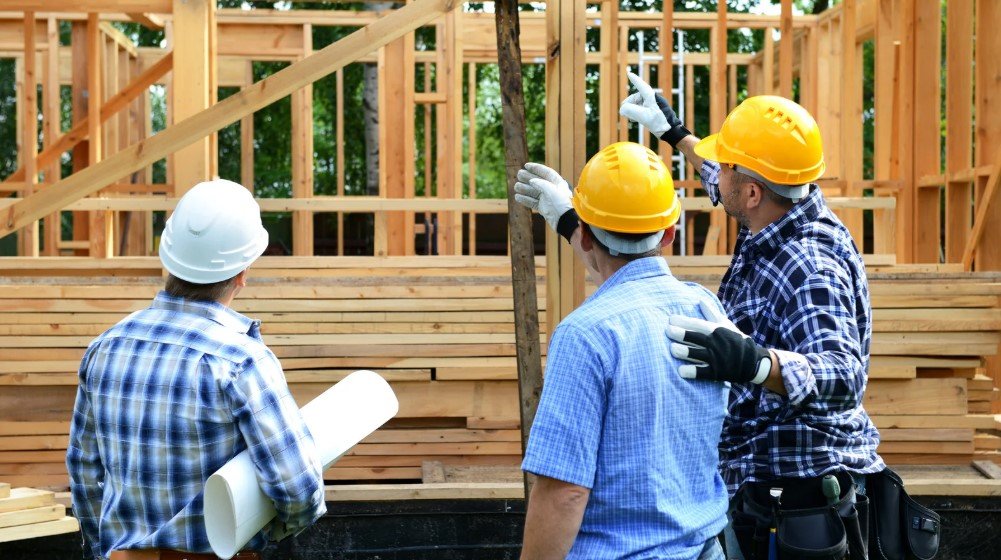 Construction workers discussing plans during a pre-construction survey on a building site, reviewing site conditions before starting construction.