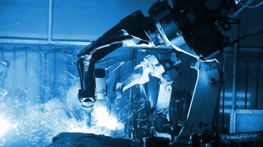 A robotic welding arm in action, creating sparks while performing automated welding in a factory setting.