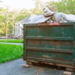 A green roll-off dumpster filled with waste, clearly marked with a "Maximum Loading Level" sign, ready for pickup during a large cleanout project.
