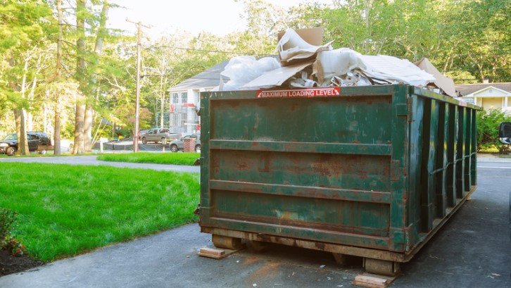 A green roll-off dumpster filled with waste, clearly marked with a "Maximum Loading Level" sign, ready for pickup during a large cleanout project.