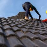 Two workers repairing a roof to prevent roof leaks, ensuring proper installation of tiles to maintain structural integrity.