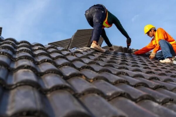 Two workers repairing a roof to prevent roof leaks, ensuring proper installation of tiles to maintain structural integrity.