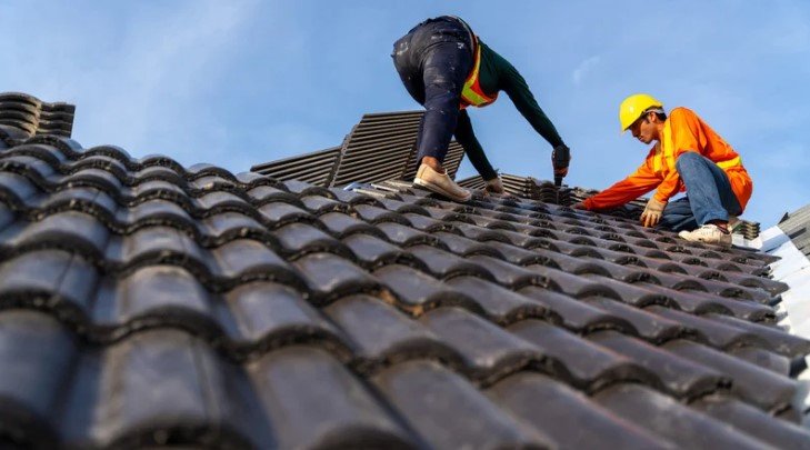 Two workers repairing a roof to prevent roof leaks, ensuring proper installation of tiles to maintain structural integrity.