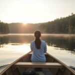 Person experiencing veneajelu, enjoying a peaceful boat ride at sunrise on a calm lake surrounded by nature in Finland