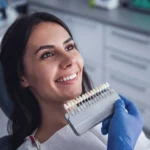 Patient in a dental office smiling as the dentist shows a set of veneer teeth shades for a smile makeover