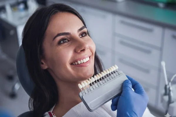 Patient in a dental office smiling as the dentist shows a set of veneer teeth shades for a smile makeover