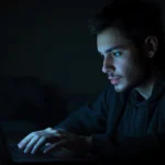 A man working late on a laptop in a dark room, reflecting search interest around lukman hakeem-mustafa seyal