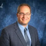Professional portrait of anthony langone martinsburg wv in suit and glasses against a blue studio background.